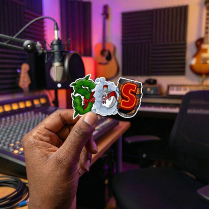 Hand holding "SOS Boat" stickers in a recording studio with musical instruments and equipment.