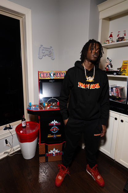 Person wearing a TSF chain and black sweatshirt with trap sauce logo in a room with nba jams retro game equipment.