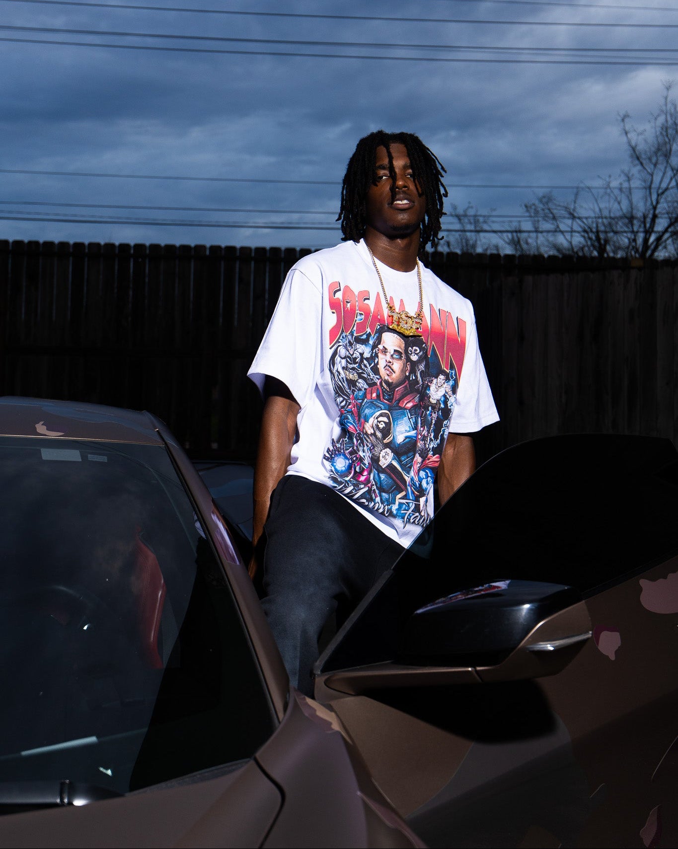 Person wearing a superhero graphic t-shirt sitting on a corvette with a dark sky background