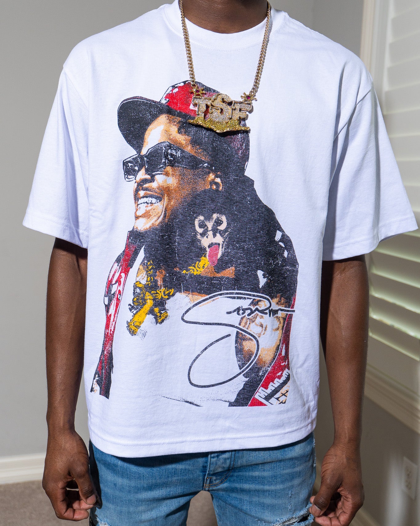 Person wearing a Tsf chain and a white t-shirt with a graphic design of a Sosamann in a hat and sunglasses.
