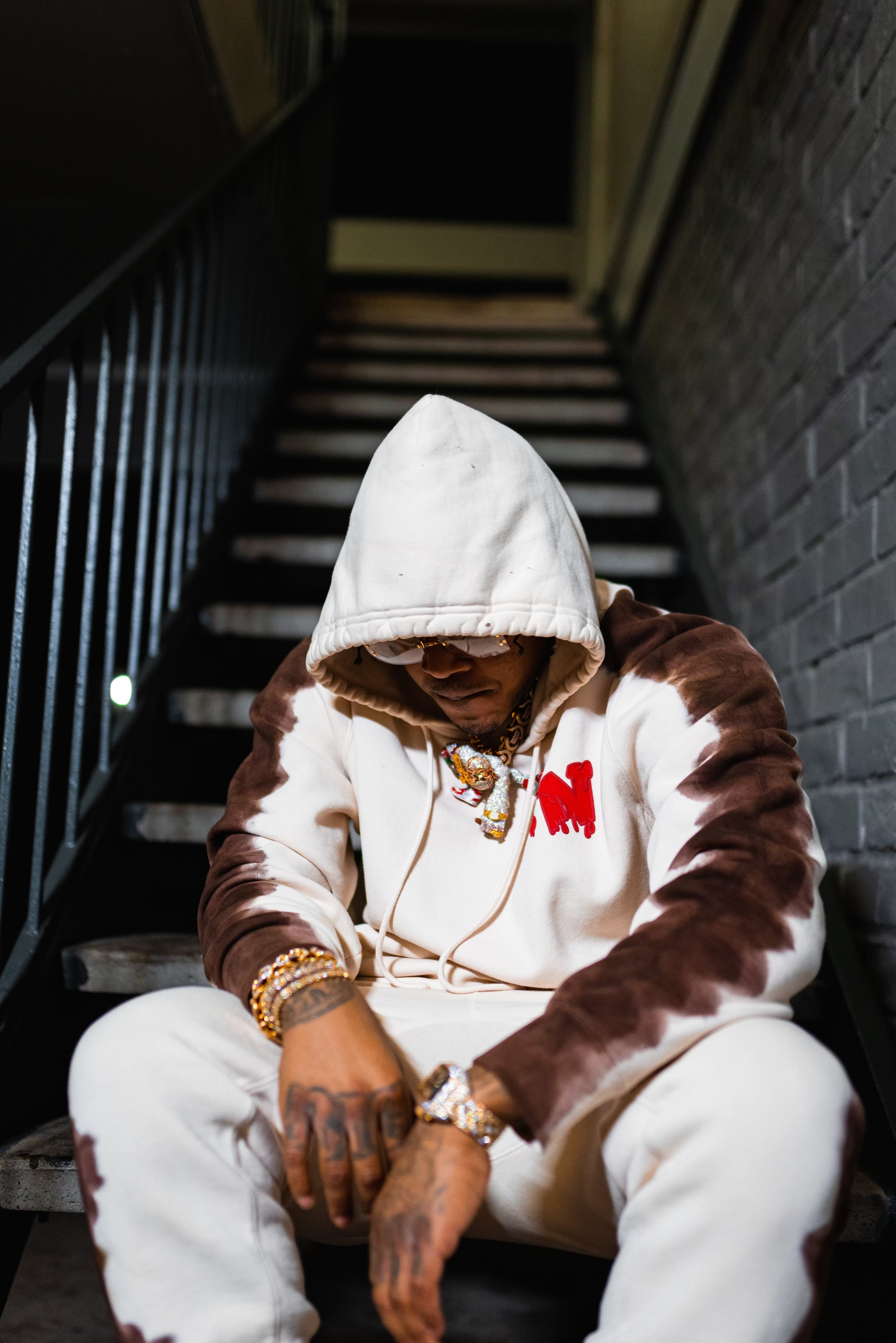 sosamnn wearing a brown and white hoodie sitting on a staircase.